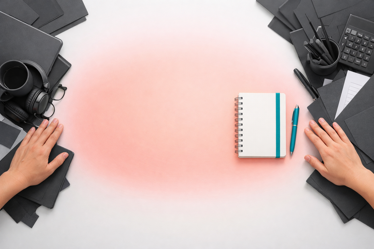 Overhead view of a bright, minimalist desk as hands push dark charcoal items aside, revealing a softly glowing coral center with a teal notebook and pen, suggesting focus and intentional simplicity.